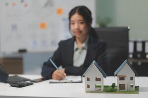 A woman in a business suit sitting at a desk with a house model photo