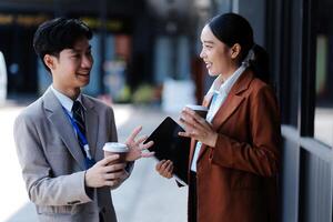 Two young people in business attire talking and holding coffee photo