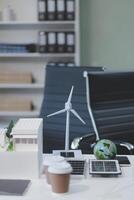 A desk with a laptop, a coffee cup, a wind turbine and a globe photo