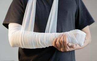 Close-up of man with bandaged hand and arm support standing over light gray color background. photo