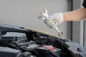 Auto mechanic holding a wrench and working on car broken engine in mechanics service or garage. photo