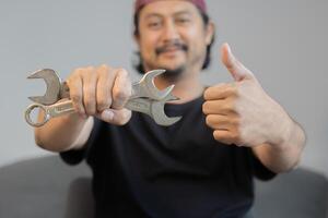 Cropped image of mechanics working in auto service. One is holding a wrench and showing Ok sign. photo