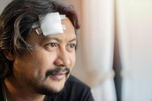 Side view portrait of happy adult Asian man with bandaged on forehead, look forward and feel better. photo