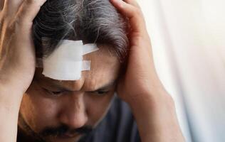 A serious Asian man has a headache and is worried from a wound on his forehead. photo