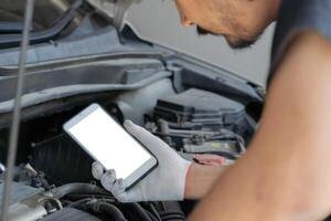 Technician man checking car engine and holding smartphone with isolate screen. Car service, repair, fixing. photo