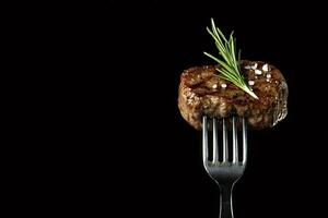 Grilled meat with rosemary and salt on a fork on black background photo