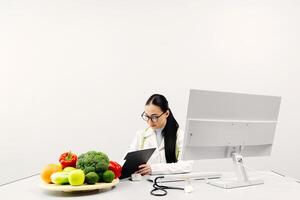 Female nutritionist working on computer at table in office. Expert makes healthy balanced diet plate according to proportions of nutrients. White background, copy space, ads photo