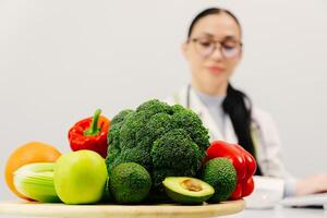 Shot of beautiful smart nutritionist woman working with computer while taking notes. Nutritionist consultation. Fresh vegetables and fruits are on the table. The concept of healthy eating. Copy space photo
