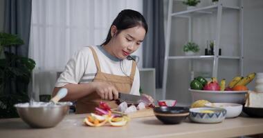 Handheld shot, Asian woman using knife to cut dragon fruit on wooden cutting board at table. video