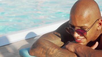 Joyful African man soaking up the sun by the shimmering swimming pool video