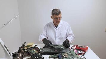 Technician Testing Laptop Motherboard with Multimeter, Electronics technician in lab coat testing a laptop motherboard using a multimeter on a workbench. video