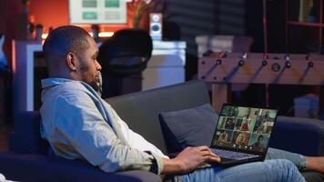Confident male speaker greeting coworkers on a web conference meeting, enjoying benefits of online remote communication in cozy loft. Black guy hosting virtual discussion. Camera B. video