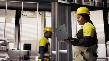 Smart factory mechanic computerizing operations and monitoring energy consumption using laptop. Repairman walking in industry 4.0 plant with notebook, providing technical support, camera A video