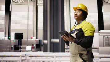 Engineer walks in photovoltaics factory, looking at system performance metrics on tablet. Worker administrates industry 4.0 plant, using device to track energy production through IoT sensors, camera A video