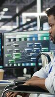 Vertical Engineer using wheelchair in data center using AI node tree software to minimize system downtime. Server hub worker in disability using visual programming to monitor performance, camera B video