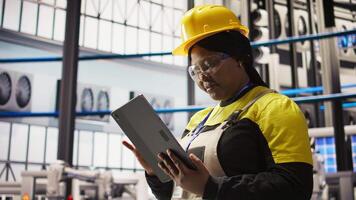 Solar panels plant expert uses tablet to oversee systems, ensuring machinery operates at optimal efficiency. Photovoltaics plant employee uses device software to maintain operations, camera A close up video