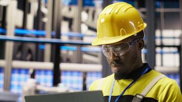 Professional working in smart factory, testing automated systems to ensure reliability. African american man in industry 4.0 plant using notebook to identify bottlenecks and optimize, camera B video