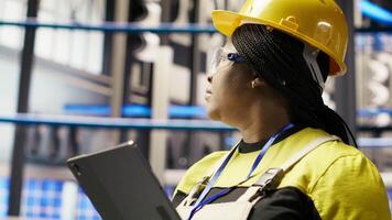 Solar panels plant expert uses tablet to oversee systems, ensuring machinery operates at optimal efficiency. Photovoltaics plant employee uses device software to maintain operations, camera B close up video