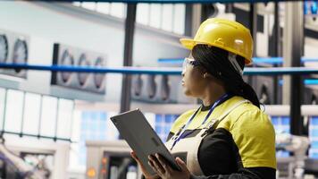Smiling engineer in smart factory performing predictive maintenance using tablet, analyzing IoT sensor data. Industrial plant worker managing operational reliability of photovoltaic systems, camera B video