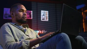 Black teleworker thinking about ways to improve his productivity, looking for new ideas for personal and professional development. Working from home on laptop, networking. Camera A. video