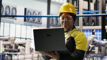 Woman working in industry 4.0 plant using notebook, following maintenance procedures. Smart factory staff member analyzing data on laptop to predict gear failures, camera B video