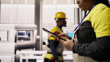 Engineer in smart factory oversees robotic assembly lines using tablet app, ensuring quality control during manufacturing. Worker monitoring automated conveyor systems using device, camera A close up video