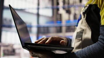 Close up of smart factory worker using laptop to test automated systems, monitoring production metrics. Industry 4.0 plant expert inspecting machinery to identify and fix malfunctions, camera A video