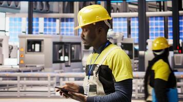 Technician in industrial plant using tablet app to diagnose equipment errors. Manufacturing factory specialist using digital device to coordinate repair tasks on assembly lines, camera A video