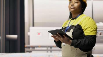 Engineer walks in photovoltaics factory, looking at system performance metrics on tablet. Worker administrates industry 4.0 plant, using device to track energy production through IoT sensors, camera B video