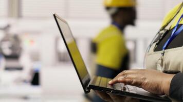 Technician in sustainable industrial plant monitors production equipment using laptop, diagnosing malfunctions. Factory worker coordinates repair tasks on solar module assembly line, camera B close up video