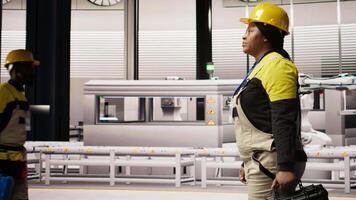 Technician walking in industrial plant, using toolbox to diagnose and fix equipment errors. African american woman in manufacturing factory coordinates repair tasks on assembly lines, camera A video