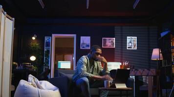 Tired black man failing some tasks and struggling to focus at home, dealing with burnout after doing overtime. Overworked fatigued person closes the laptop and taking a break. Camera A. video