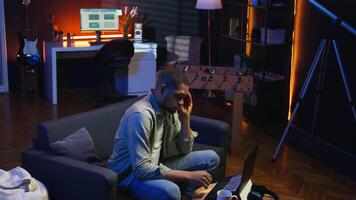 African american person receiving some bad news while doing remote work tasks, feeling overworked and under pressure to complete all his assignments. Young adult deals with burnout. Camera A. video