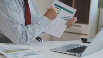 A man in a business suit is looking at a document on his laptop video