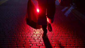Legs of Santa Claus. Father Frost carrying presents at Christmas in red bag outdoors. Black boots of Santa walking on a pavement at dark on snow background. Red light. video