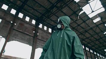 Human in a respirator and a hood is standing in abandoned building. Survivor on the background of a ruined building with holes on roof. video