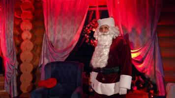 Bearded Santa Claus in cosy room with Christmas tree. Portrait of Santa looking on camera on the background of a New year tree and a fireplace. Red evening light. video