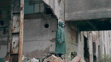 Survivor in abandoned place with radiation. Virologist man in protective costume and respirator gas mask stands in a deserted industrial factory background. video