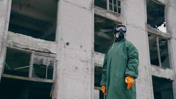 Man in protective clothing and a gas mask is standing on the background of ruined building. The concept of a post-apocalyptic world. video