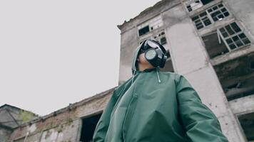Woman in respirator and protective coat. Survivor on the background of ruined building without windows, Chemical pollution in the city. View from below. video