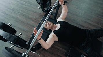 Strong healthy bodybuilder exercising in gym. Handsome guy lifting barbell while laying on a simulator. Top view. Sports concept. video