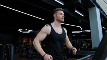 Young handsome man training on a simulator. Athletic guy is running on a modern treadmill in the gym. Slow motion. video