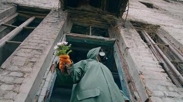 Ecologist in ruined building. Person in protective suit and gas mask with bunch of flowers. Air pollution in chemical zone. View from below. video