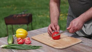Man cutting tomato on a board outdoors. Preparing dinner at dacha. Man cuts vegetable into four parts on a table before the picnic. video