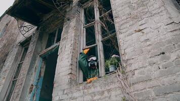 Ecologist wearing respirator alone in empty house. Man in safety suit and mask looking out of the window without glass from abandoned building. Chemical attack. video