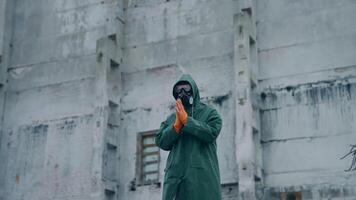 Man in protective suit and mask in infected zone. Person wearing respirator and safety uniform, in protective gloves standing on the background of abandoned building. video