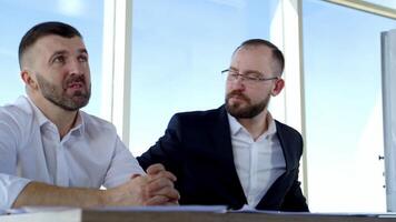 Portrait of two businessmen talking in office. Serious partners discussing business strategy indoors on window background at daytime. Business concept. video