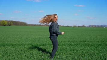Happy girl in jeans on a green meadow. Beautiful young woman jumping joyfully on a field in a bright day. Cheerful model among nature. video