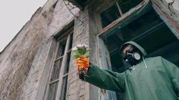 Flowers in hand of an ecologist in protective suit. Person in respirator and hazmat wearing standing with flowers in ruined place. Nature in danger. video
