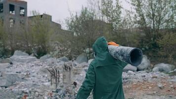Man in safety suit walking in dangerous zone. Human in protective uniform and respirator is carrying pipe in the abandoned place with polluted air. Rear view. video